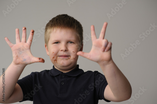 a fair-haired boy of 8 years old with a chocolate-stained face shows his age on his fingers on his birthday