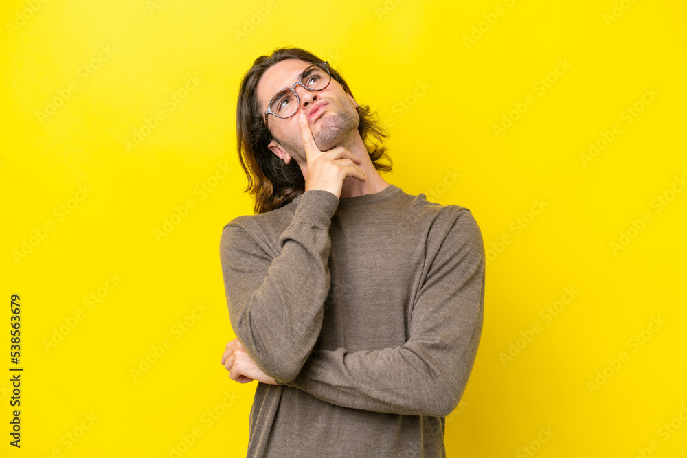 Caucasian handsome man isolated on yellow background having doubts while looking up Caucasian handsome man isolated on yellow background having doubts while looking up