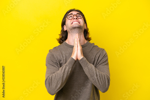Obraz na plátně Caucasian handsome man isolated on yellow background keeps palm together