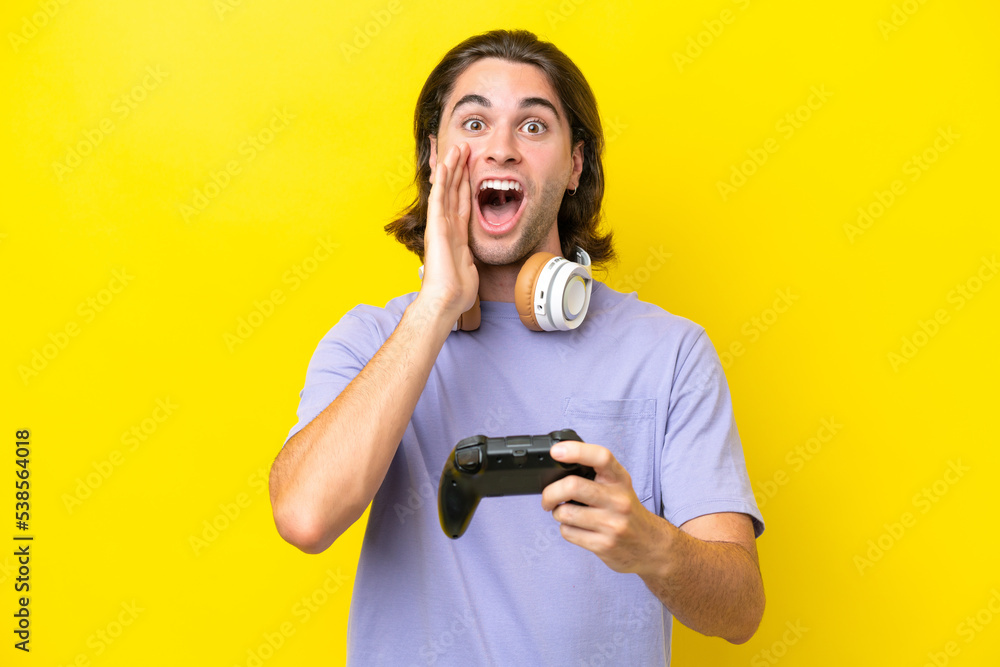 Young handsome caucasian man playing with a video game controller over isolated on yellow background with surprise and shocked facial expression Young handsome caucasian man playing with a video game controller over isolated on yellow background with surprise and shocked facial expression
