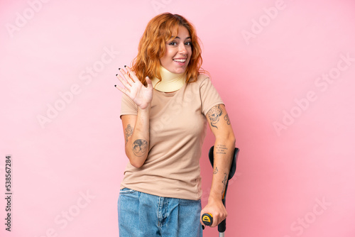 Young caucasian woman wearing neck brace isolated on pink background saluting with hand with happy expression