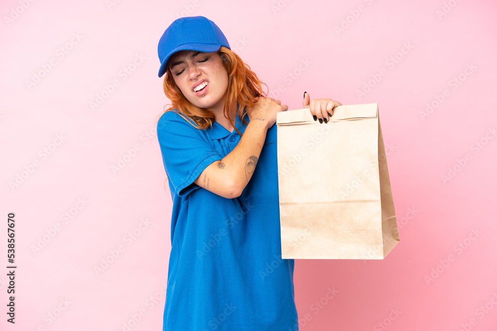 Fototapeta premium Young caucasian woman taking a bag of takeaway food isolated on pink background suffering from pain in shoulder for having made an effort