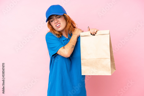 Young caucasian woman taking a bag of takeaway food isolated on pink background suffering from pain in shoulder for having made an effort