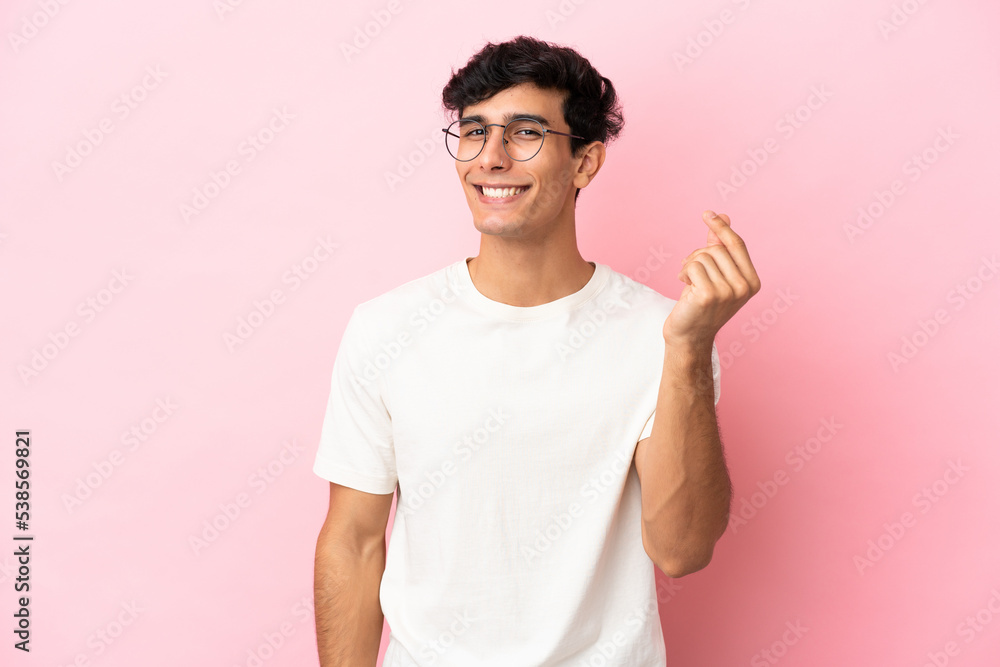 Young Argentinian man isolated on pink background making money gesture Young Argentinian man isolated on pink background making money gesture