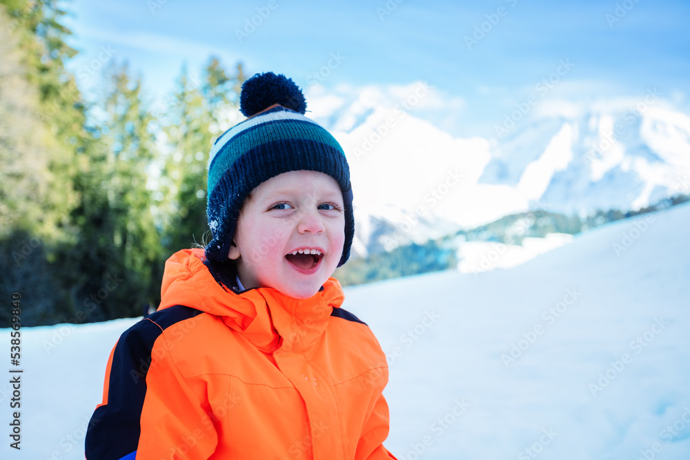Laughing young boy in winter outfit outside over snow mountains Laughing young boy in winter outfit outside over snow mountains