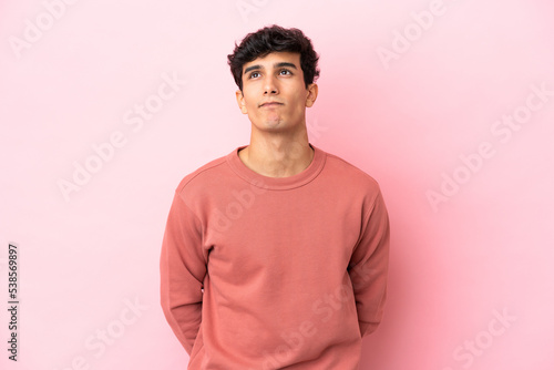 Young Argentinian man isolated on pink background and looking up © luismolinero