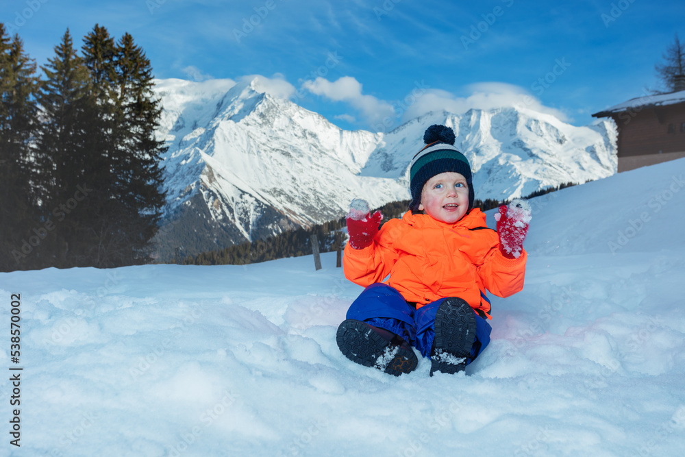 Boy in winter outfit play with snow at mountains on background Boy in winter outfit play with snow at mountains on background