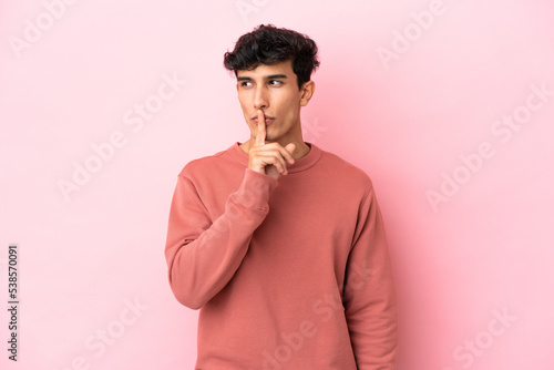 Young Argentinian man isolated on pink background showing a sign of silence gesture putting finger in mouth