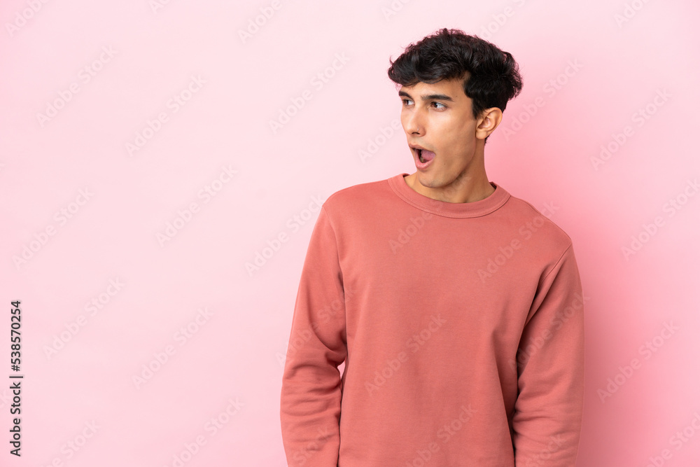 Young Argentinian man isolated on pink background doing surprise gesture while looking to the side Young Argentinian man isolated on pink background doing surprise gesture while looking to the side