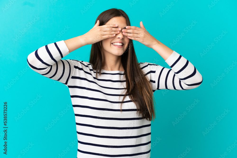 Teenager Brazilian girl over isolated blue background covering eyes by hands and smiling Teenager Brazilian girl over isolated blue background covering eyes by hands and smiling