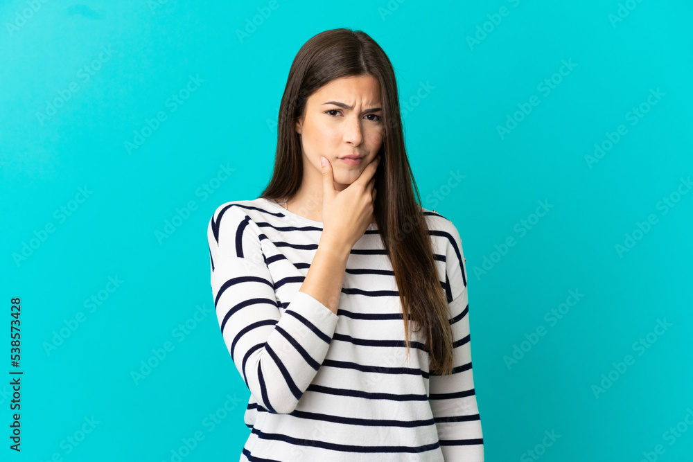 Teenager Brazilian girl over isolated blue background having doubts Teenager Brazilian girl over isolated blue background having doubts