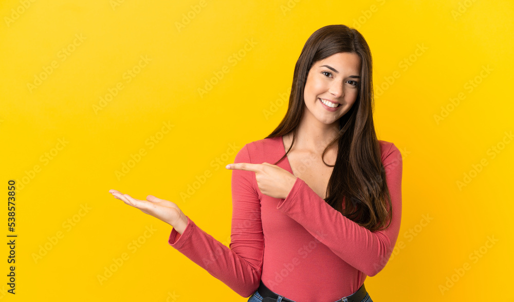 Teenager Brazilian girl over isolated yellow background holding copyspace imaginary on the palm to insert an ad Teenager Brazilian girl over isolated yellow background holding copyspace imaginary on the palm to insert an ad