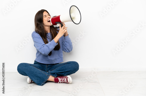 Young woman sitting on the floor shouting through a megaphone