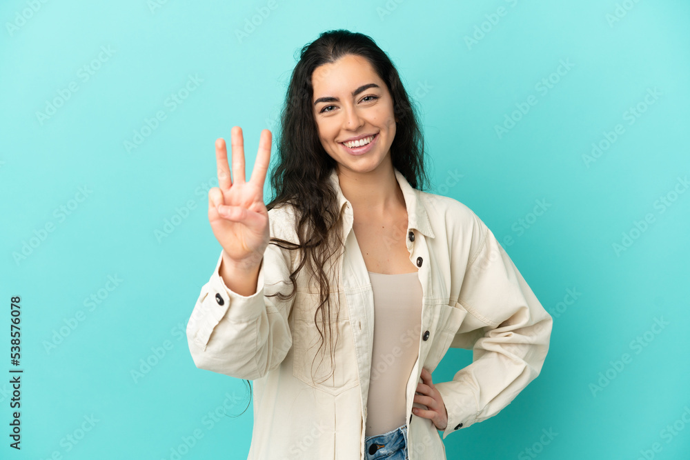 Young caucasian woman isolated on blue background happy and counting three with fingers Young caucasian woman isolated on blue background happy and counting three with fingers