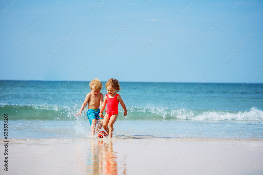 Cute little boy and a girl play ball in the ocean waves