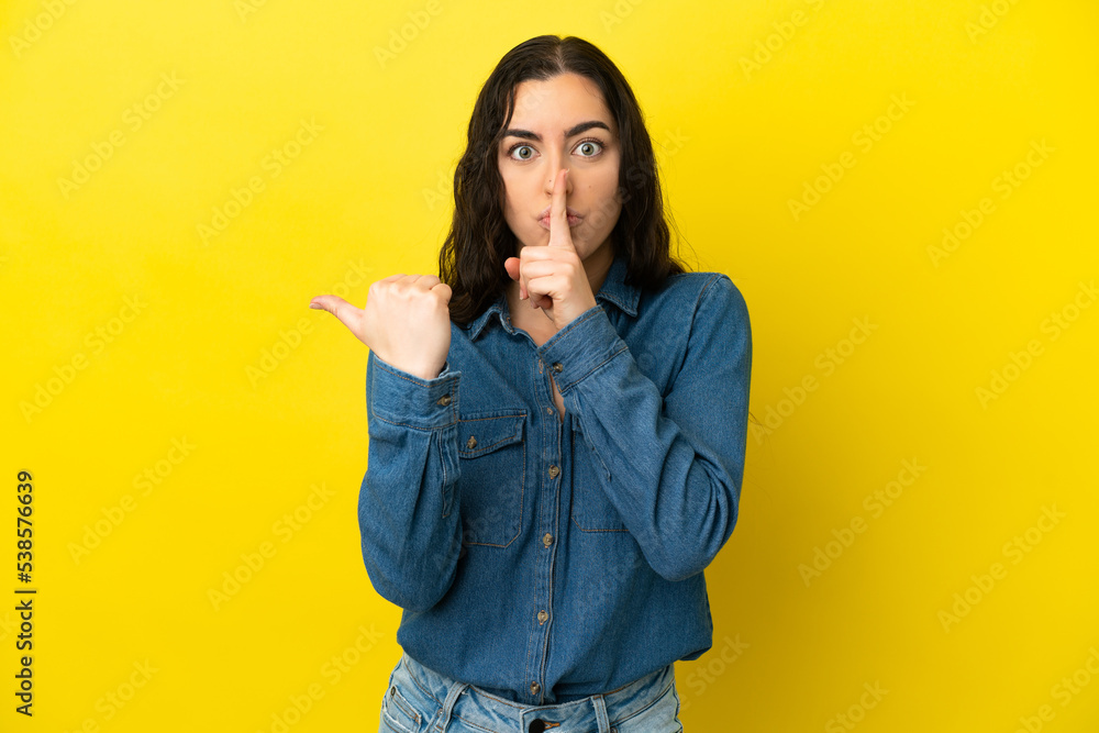 Young caucasian woman isolated on yellow background pointing to the side and doing silence gesture Young caucasian woman isolated on yellow background pointing to the side and doing silence gesture