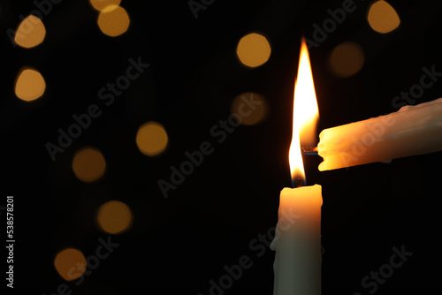 Konstfotografi Lighting candle from another one against blurred lights in darkness, closeup