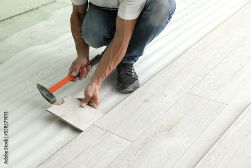 Man using hammer during installation of new laminate flooring, closeup