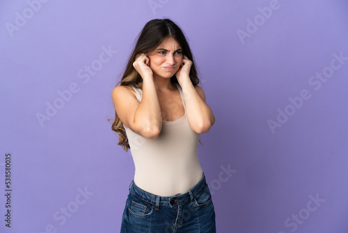 Young caucasian woman isolated on purple background frustrated and covering ears © luismolinero