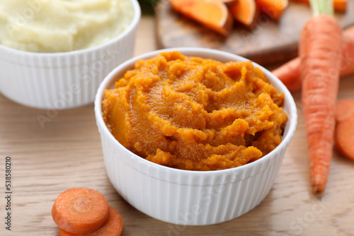 Bowl with tasty carrot puree and ingredients on wooden table, closeup photo