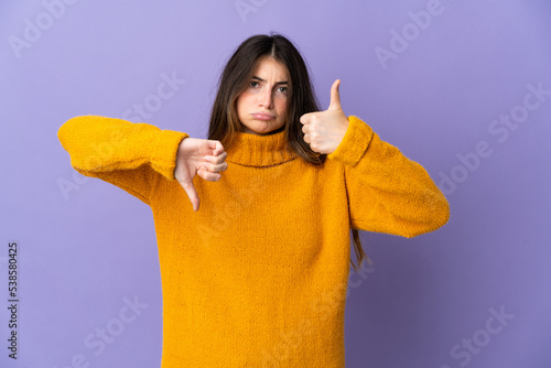 Young caucasian woman isolated on purple background making good-bad sign. Undecided between yes or not © luismolinero