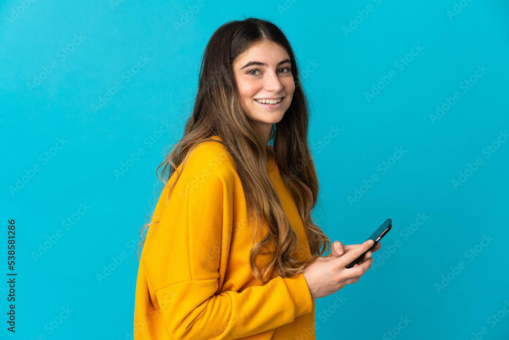 Young caucasian woman isolated on blue background sending a message or email with the mobile Young caucasian woman isolated on blue background sending a message or email with the mobile