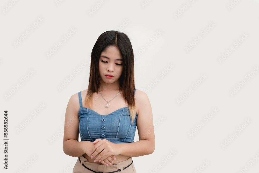 A female teenager looks down and frowns at the ground as she demonstrates a body language of a sad expression. Studio shot isolated on white background. A female teenager looks down and frowns at the ground as she demonstrates a body language of a sad expression. Studio shot isolated on white background.