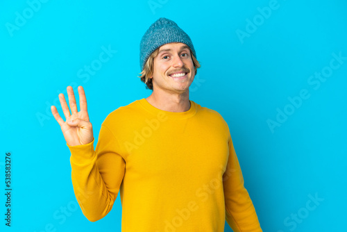 Handsome blonde man isolated on blue background saluting with hand with happy expression