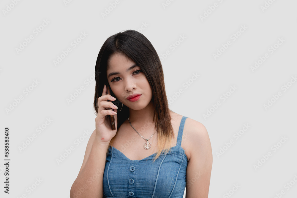 An Asian young woman puts on a serious look while speaking on the phone with her boyfriend. Isolated on white background studio shot.