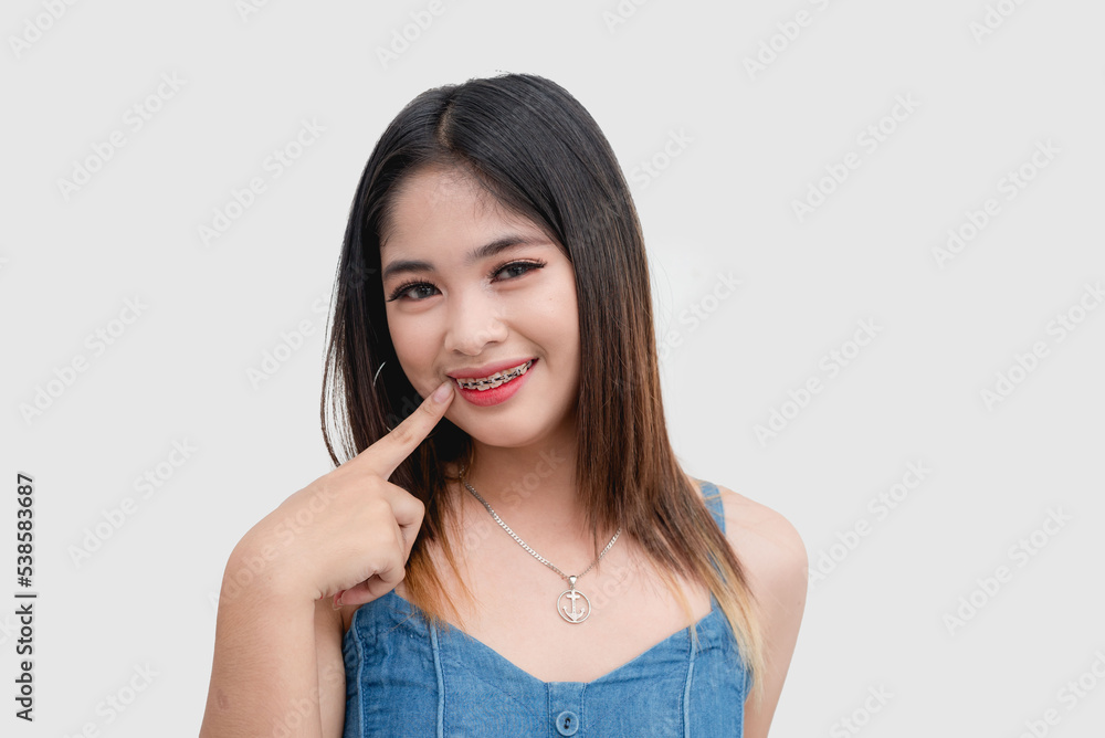 A beautiful and smiling Filipina points at her teeth as she shows her braces to the camera. Studio shot isolated on white background. A beautiful and smiling Filipina points at her teeth as she shows her braces to the camera. Studio shot isolated on white background.