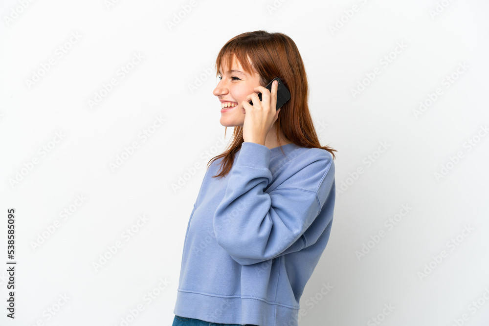 Redhead girl isolated on white background keeping a conversation with the mobile phone with someone Redhead girl isolated on white background keeping a conversation with the mobile phone with someone