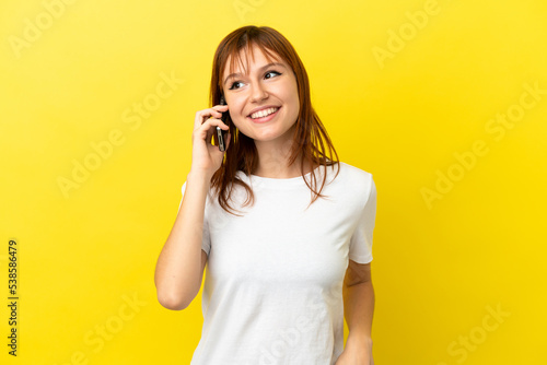 Redhead girl isolated on yellow background keeping a conversation with the mobile phone with someone © luismolinero