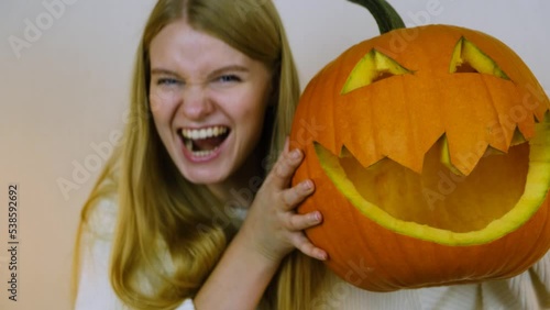 Close-up. The girl picks up a pumpkin. The camera follows the pumpkin. The girl holds a pumpkin next to her head. The girl grimaces along with the pumpkin. Halloween. 4k.