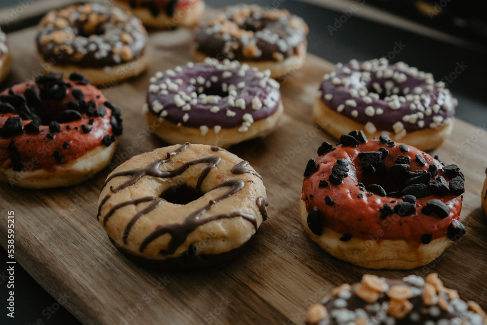 conjunto de donuts de diferentes colores con chocolate y azúcar encima de una tabla de madera
