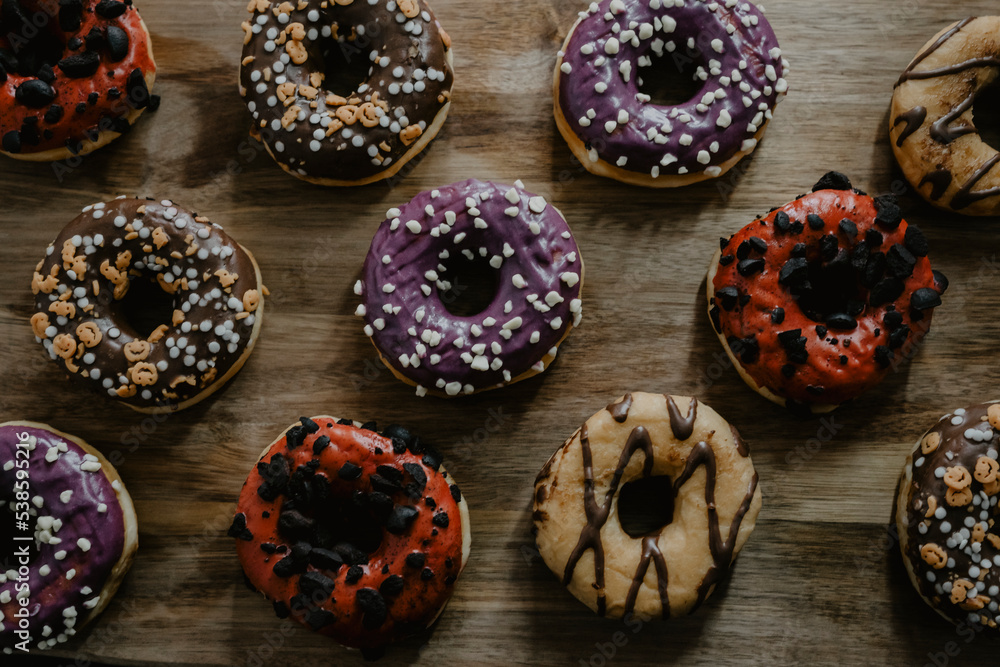 Fototapeta premium conjunto de donuts de diferentes colores con chocolate y azúcar encima de una tabla de madera