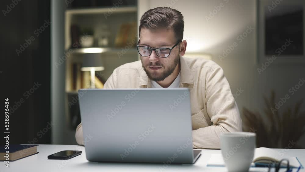 Young caucasian businessman working at home with laptop and papers on desk in the evening Young caucasian businessman working at home with laptop and papers on desk in the evening