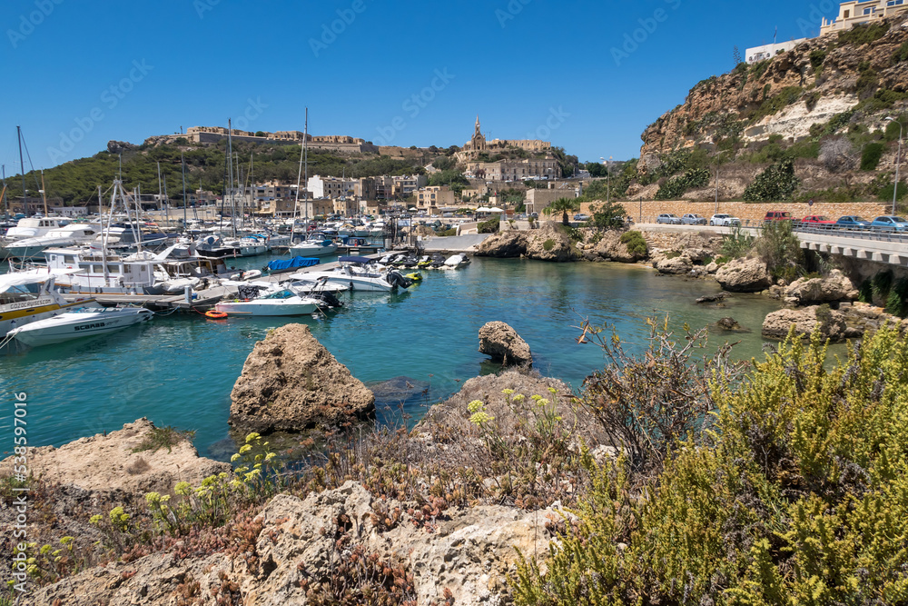 Beautiful shoreline on Gozo, Malta with boats anchored. Summer weather with clear blue sky.