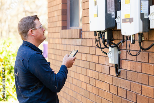 Electrician troubleshooting solar power box on wall of home using phone photo