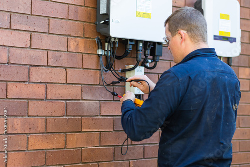 Electrician tradie using multimeter tool to check power in solar system installation photo