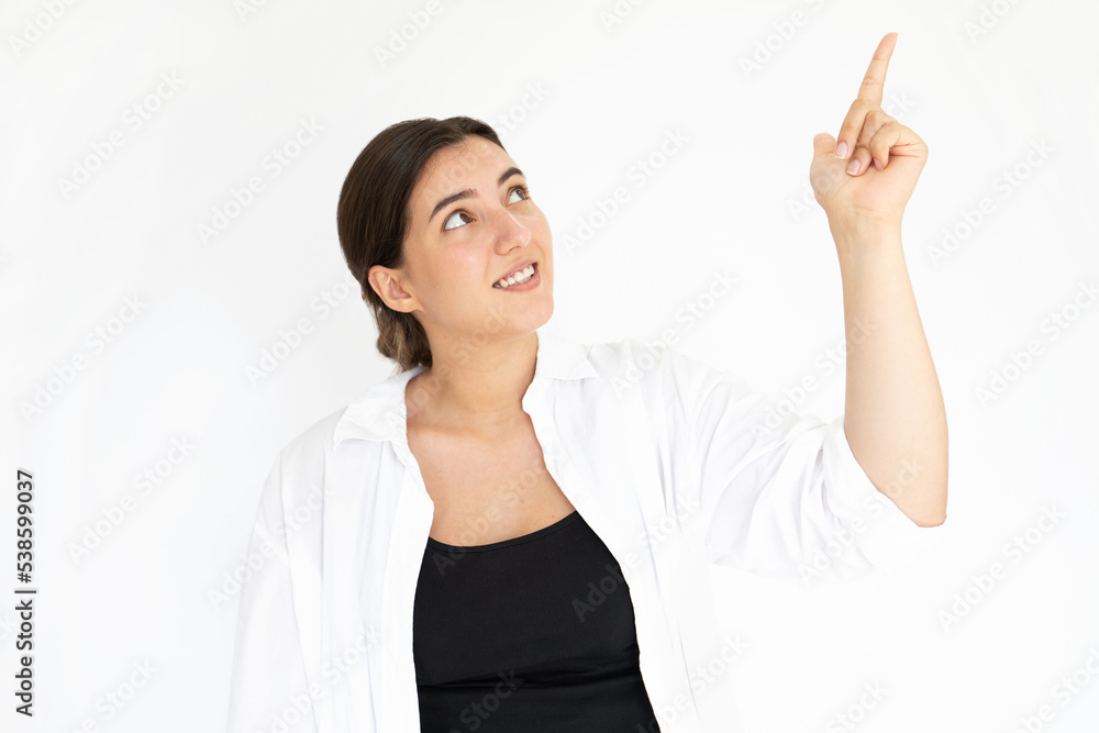 Portrait of happy young woman pointing upwards and smiling. Caucasian lady wearing black top and white T-shirt showing something against white background. Advertising concept Portrait of happy young woman pointing upwards and smiling. Caucasian lady wearing black top and white T-shirt showing something against white background. Advertising concept