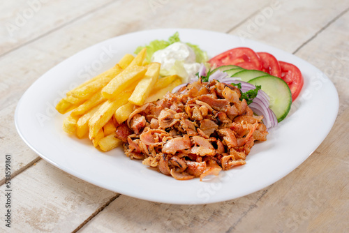 Doner kebab or gyros. Chicken meat on a white plate with salad and french fries. Copy space for text. Wooden background