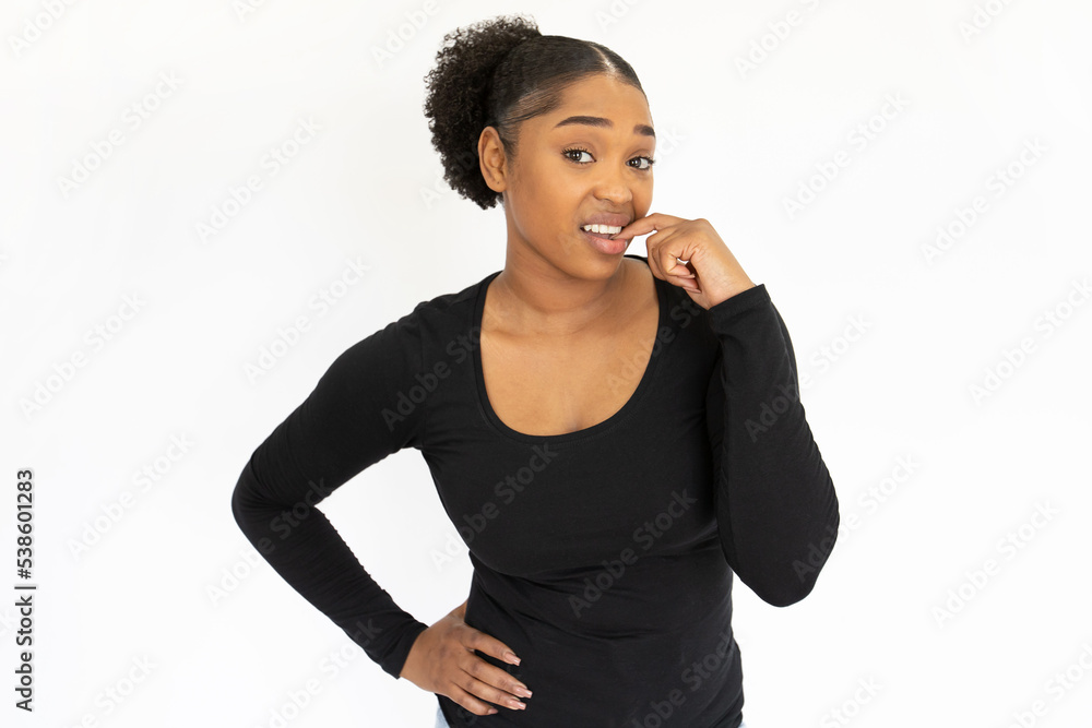 Portrait of nervous young woman biting fingernail. African American lady wearing black longsleeve standing with hand on hip and looking at camera with doubt. Indifference and uncertainty concept
