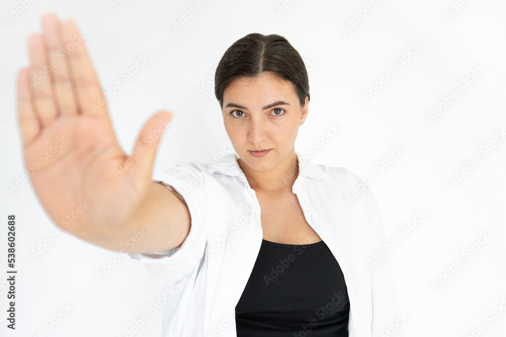Portrait of serious young woman making stop gesture. Caucasian lady wearing black top and white T-shirt looking at camera making warning sign against white background. Refusal and forbiddance concept Portrait of serious young woman making stop gesture. Caucasian lady wearing black top and white T-shirt looking at camera making warning sign against white background. Refusal and forbiddance concept