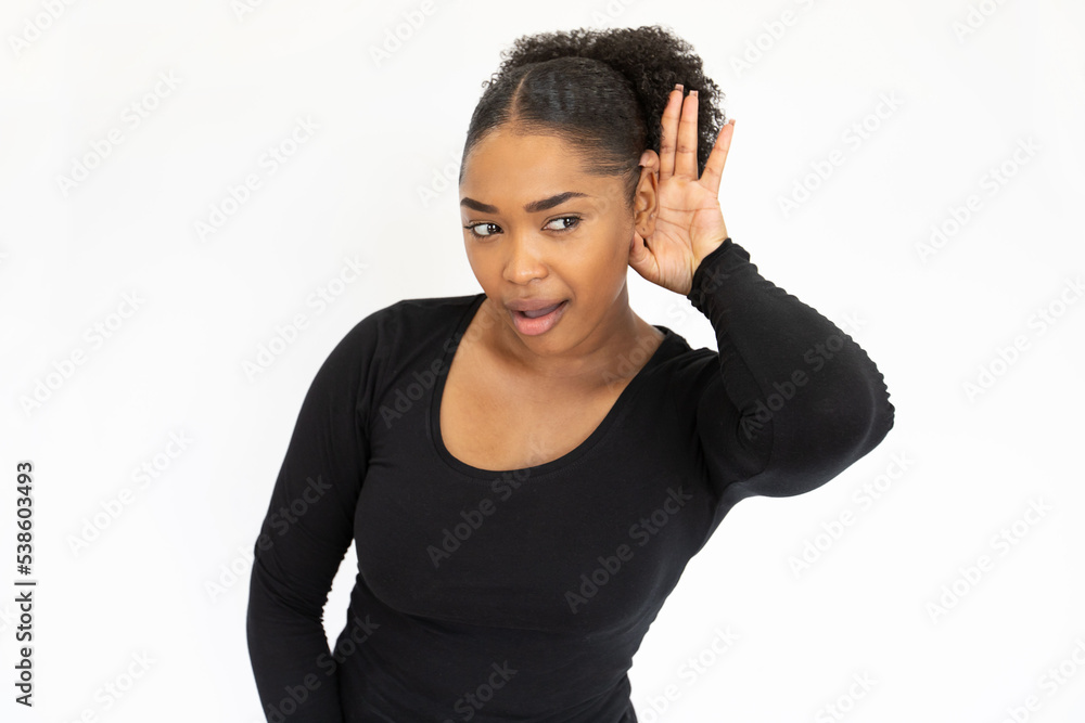 Portrait of concentrated young woman straining ears against white background. African American lady wearing black longsleeve listening to gossip with hand at ear. Hearing problem and gossip concept Portrait of concentrated young woman straining ears against white background. African American lady wearing black longsleeve listening to gossip with hand at ear. Hearing problem and gossip concept