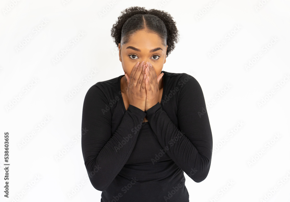 Portrait of shocked young woman covering mouth with hand. African American lady wearing black longsleeve looking at camera with shame or fear against white background. Shock and problem concept Portrait of shocked young woman covering mouth with hand. African American lady wearing black longsleeve looking at camera with shame or fear against white background. Shock and problem concept