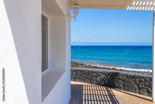 Seascape from the window. White house with a pergola and big sea view windows. Perspective lines leading to the blue sea. Summer vacations beach house. There is copy space for design.