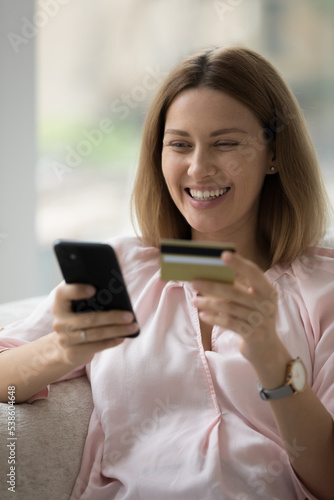 Vertical image happy woman buying goods and electronic services using smartphone and credit card, enjoy remote on-line purchase, transfer funds use mobile application, making order distantly at home