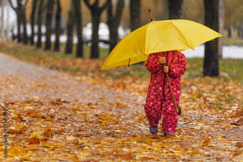 Little child in autumn park. Child hid behind large yellow umbrella and walks on the fallen leaves.