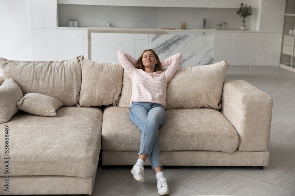 Full length view peaceful woman in casual clothes leaned on sofa cushions relaxing alone indoor, female enjoy break and fresh air at modern home, having stress-free weekend, relish day off at own flat Full length view peaceful woman in casual clothes leaned on sofa cushions relaxing alone indoor, female enjoy break and fresh air at modern home, having stress-free weekend, relish day off at own flat