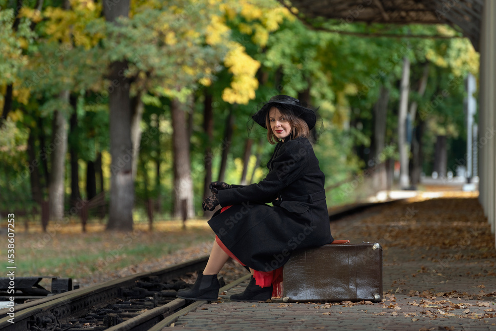Middle-aged woman with retro suitcase at the train station waiting for train. Style 30-40s. Vintage clothes, autumn Middle-aged woman with retro suitcase at the train station waiting for train. Style 30-40s. Vintage clothes, autumn